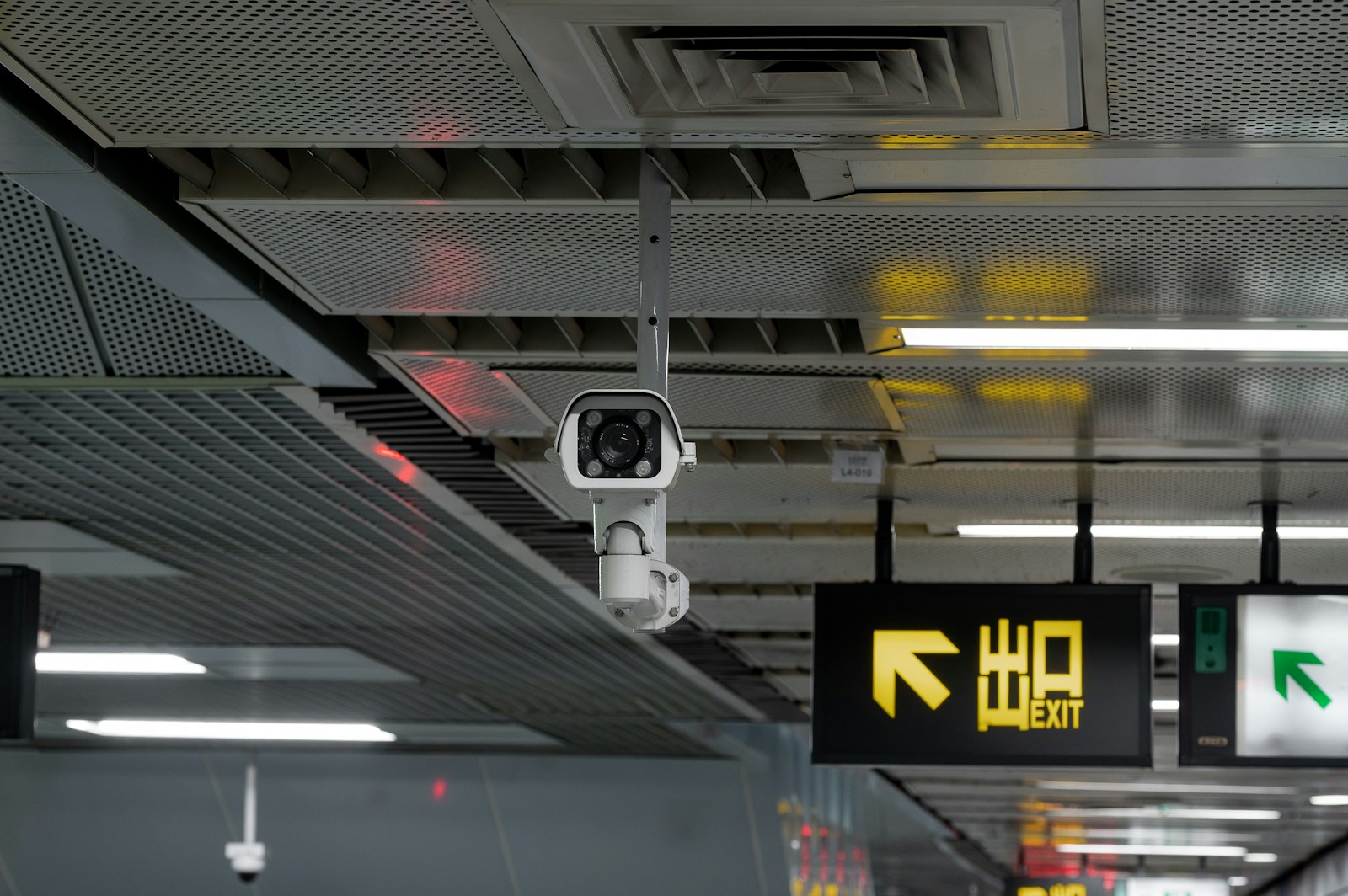 Security camera mounted on a ceiling with exit sign.
